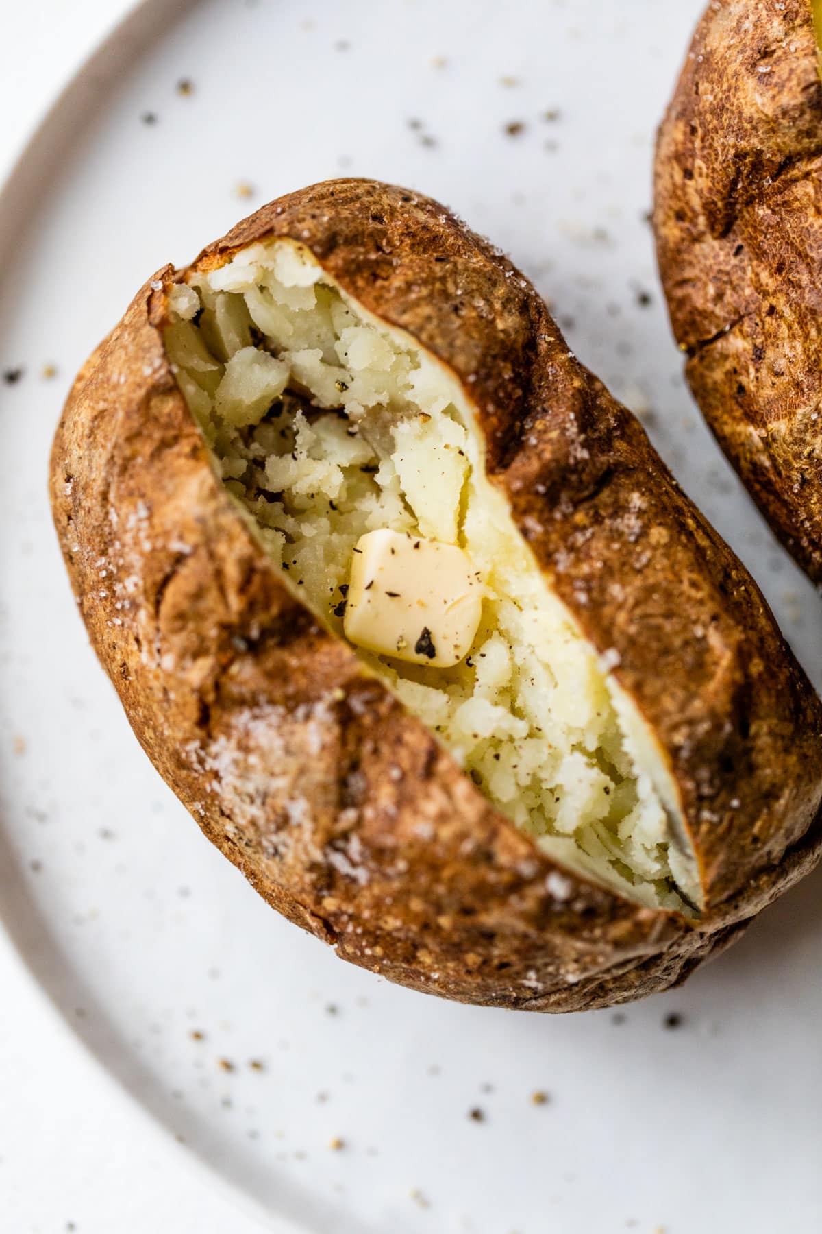 An air fryer baked potato with butter on a plate